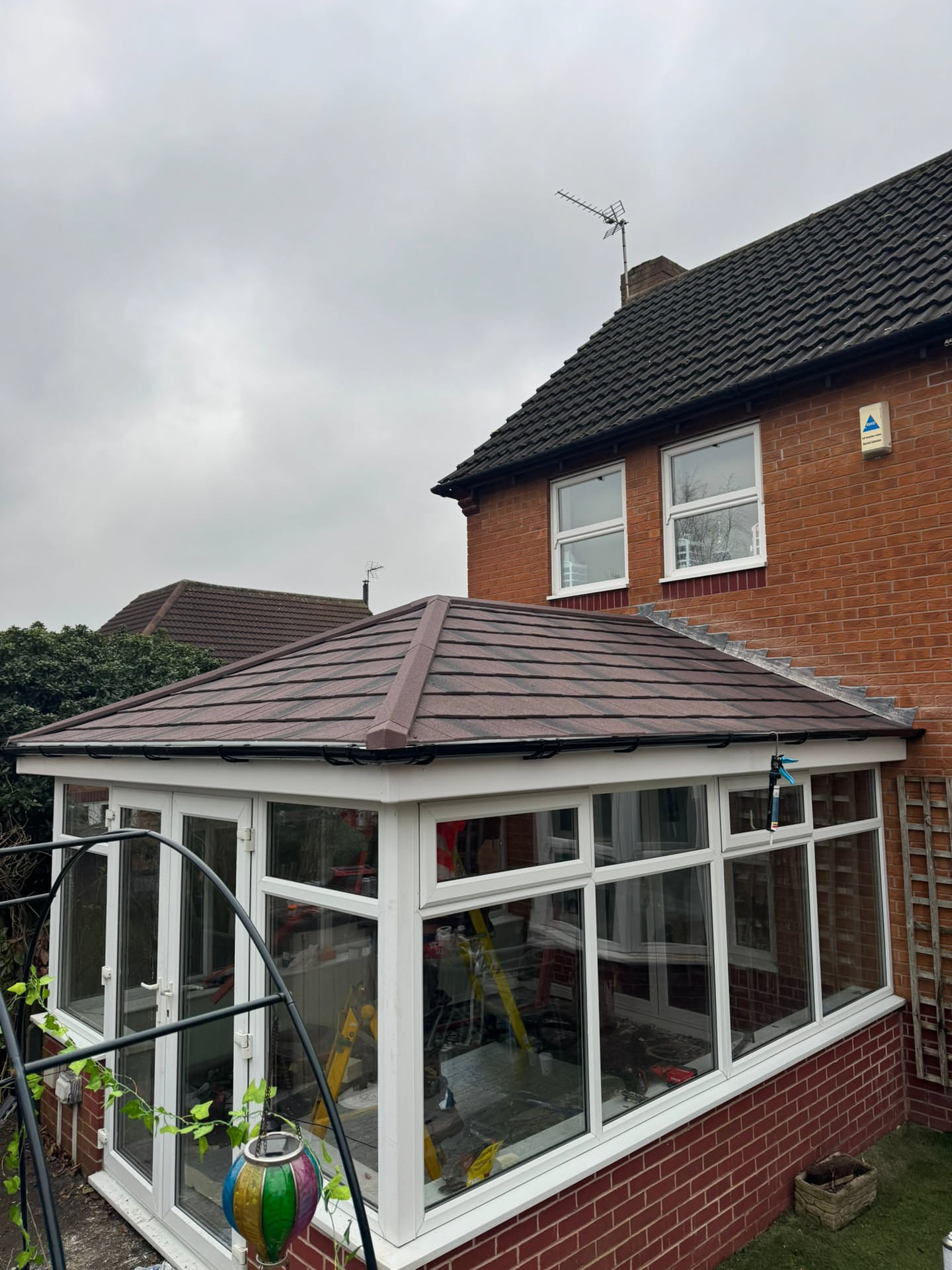 Brown tiled conservatory roof with white uPVC frames on brick house